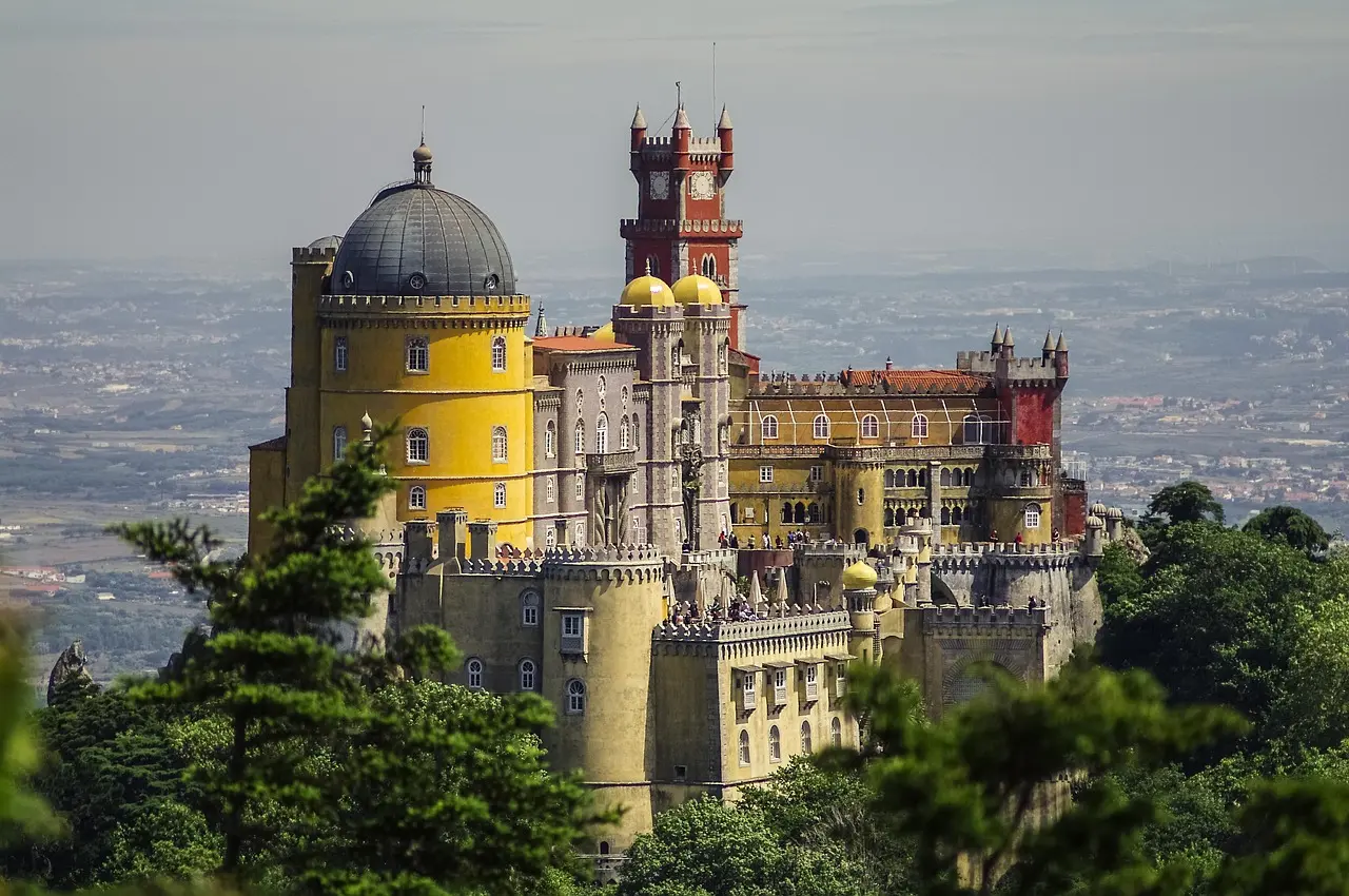 Casal caminhando de mãos dadas pelas ruas de paralelepípedos de Sintra, com castelo ao fundo.