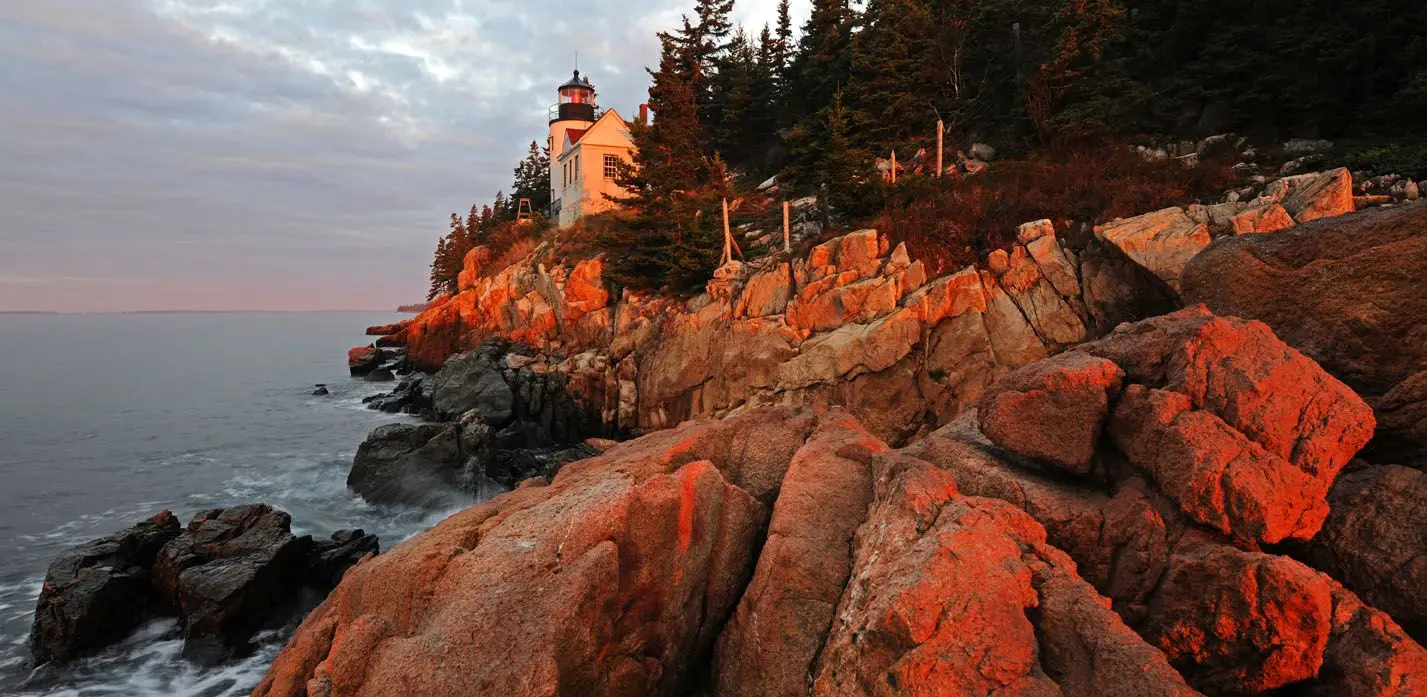 Farol em Acadia National Park com ondas quebrando nas rochas ao amanhecer
