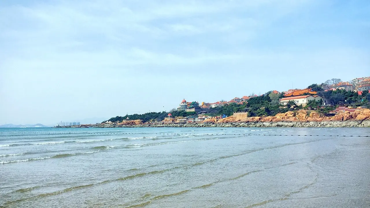 Praia de Badaguan em Qingdao com casas coloniais alemãs ao fundo e mar azul-turquesa.