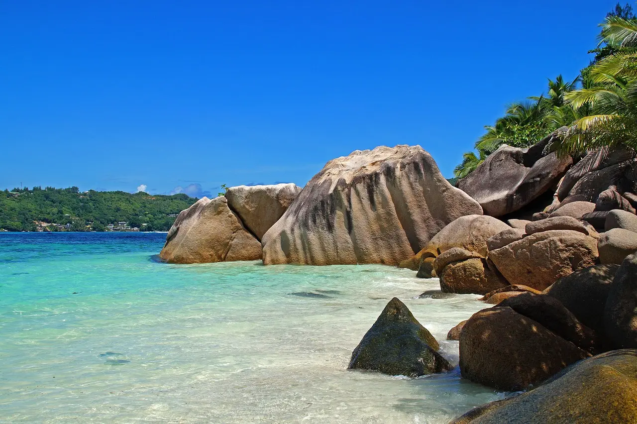 Praia deserta nas Seychelles com rochas gigantes e coqueiros refletidos na água cristalina.