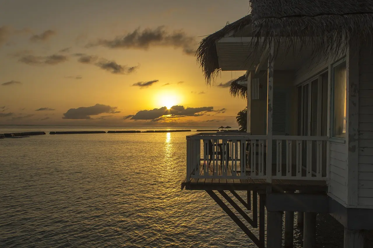 Suíte sobre a água nas Maldivas com deck privativo e vista para o oceano Índico ao amanhecer.