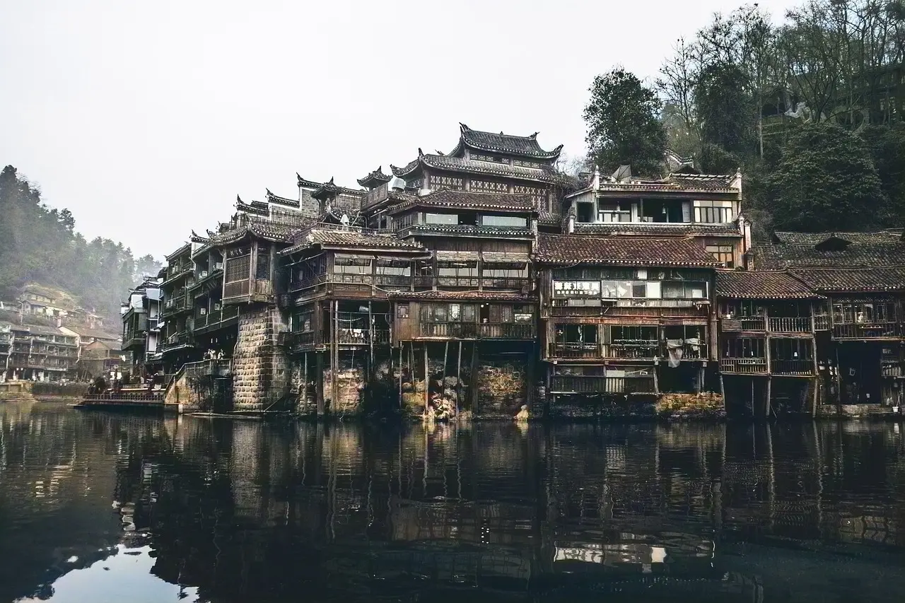 Casas sobre palafitas em Fenghuang refletidas no Rio Tuojiang, com pontes arqueadas e lanternas vermelhas.