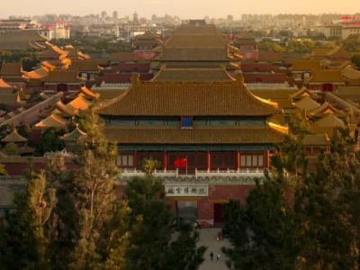 Vista aérea da Cidade Proibida em Pequim ao pôr do sol, com telhados dourados brilhando sob a luz suave.