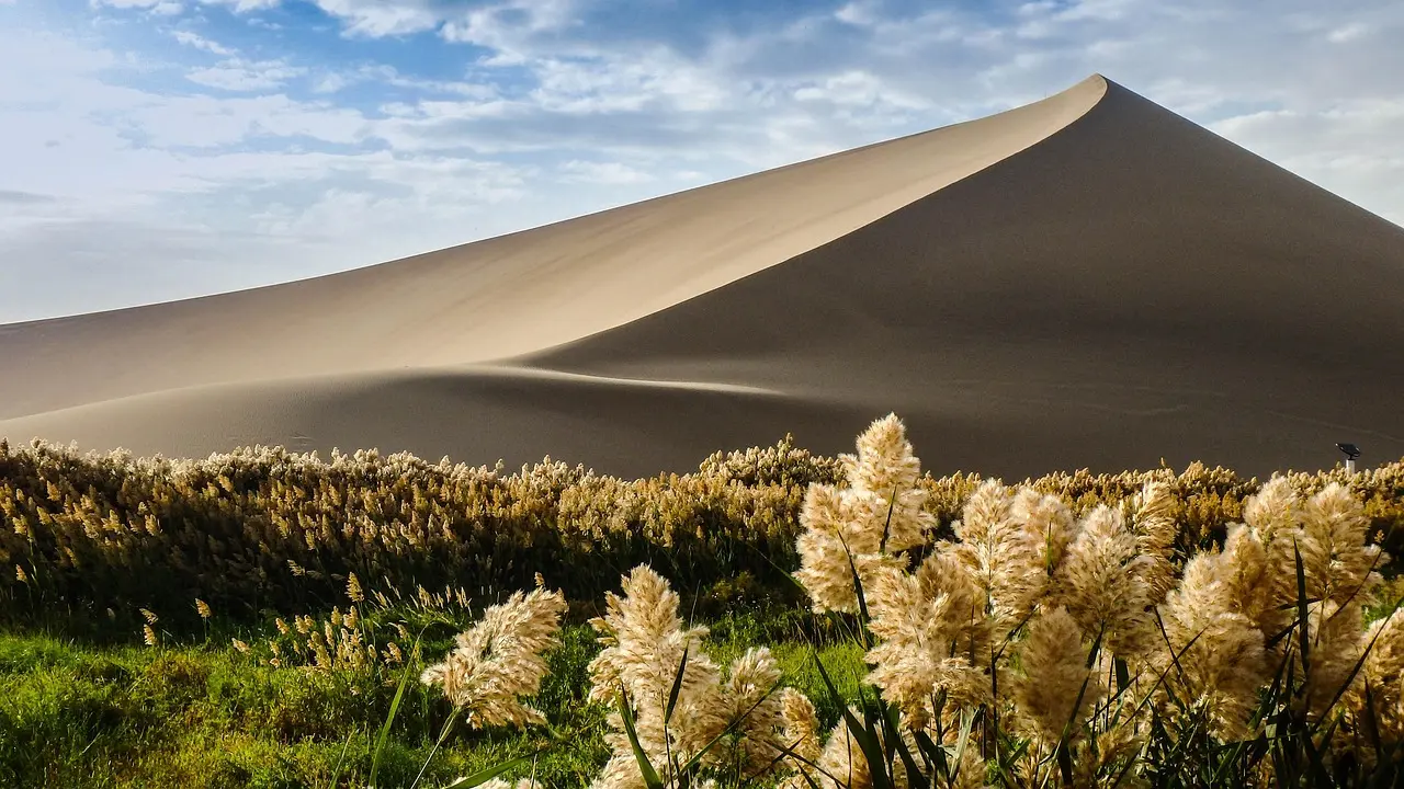 Dunas de areia dourada no Deserto de Gobi perto de Dunhuang, com Oásis de Crescent Moon Lake ao fundo.