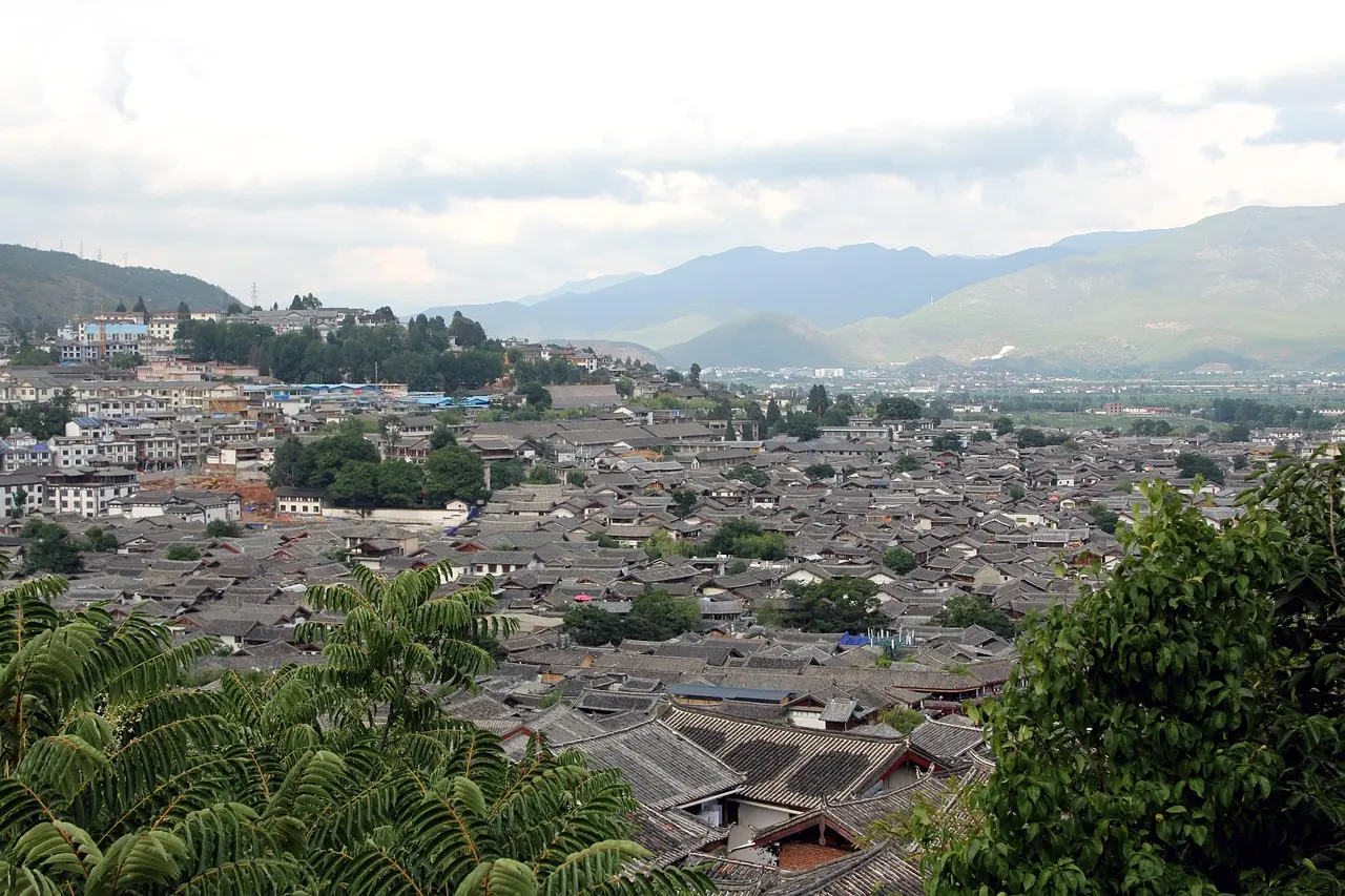 Ruas de paralelepípedos e canais na Cidade Antiga de Lijiang, com montanhas nevadas ao fundo.